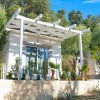 Una piccola casa bianca con tettoia, circondata da piante verdi.